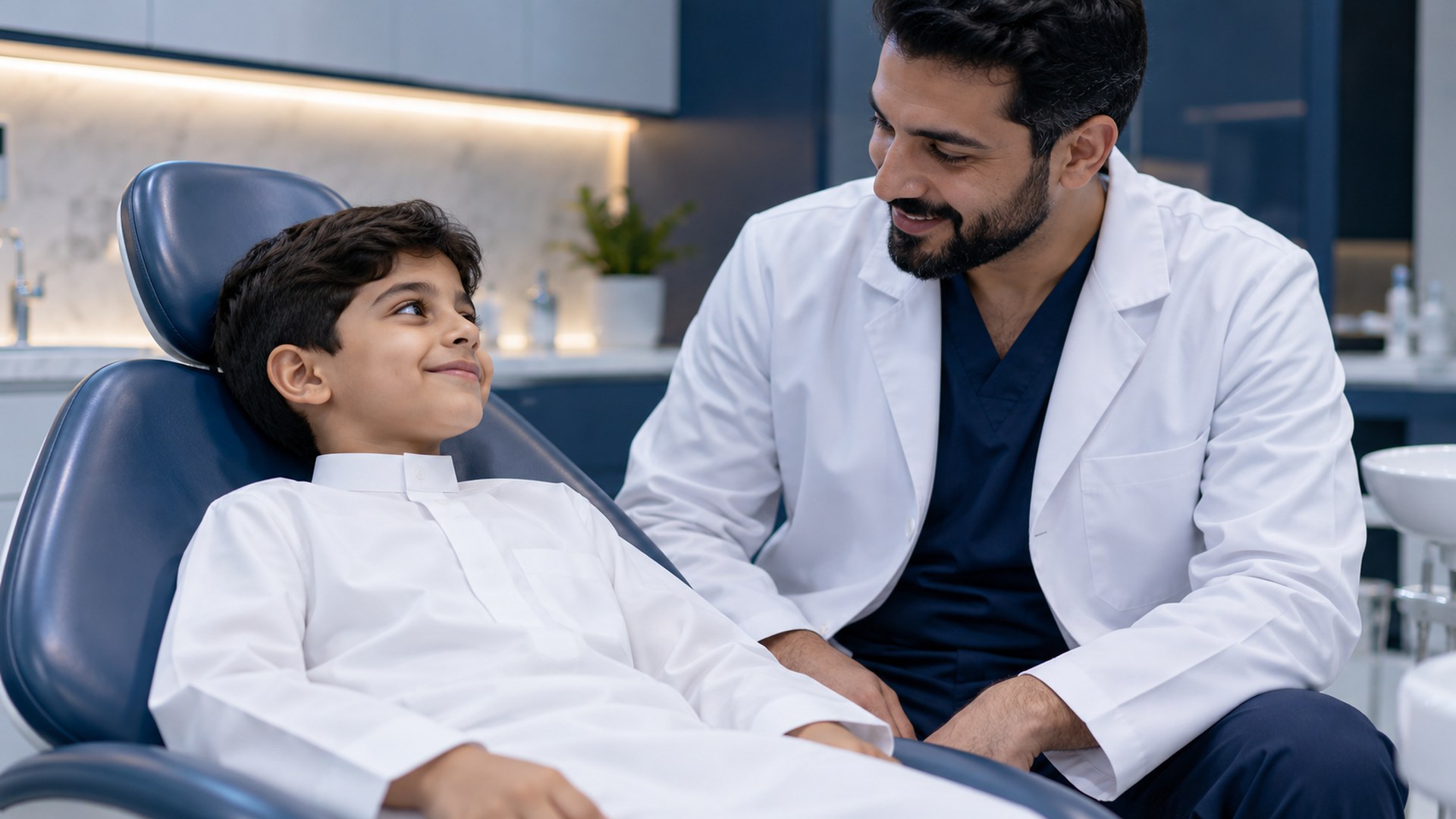 طفل خليجي مرتاح على كرسي الأسنان بجانب طبيب منتبه