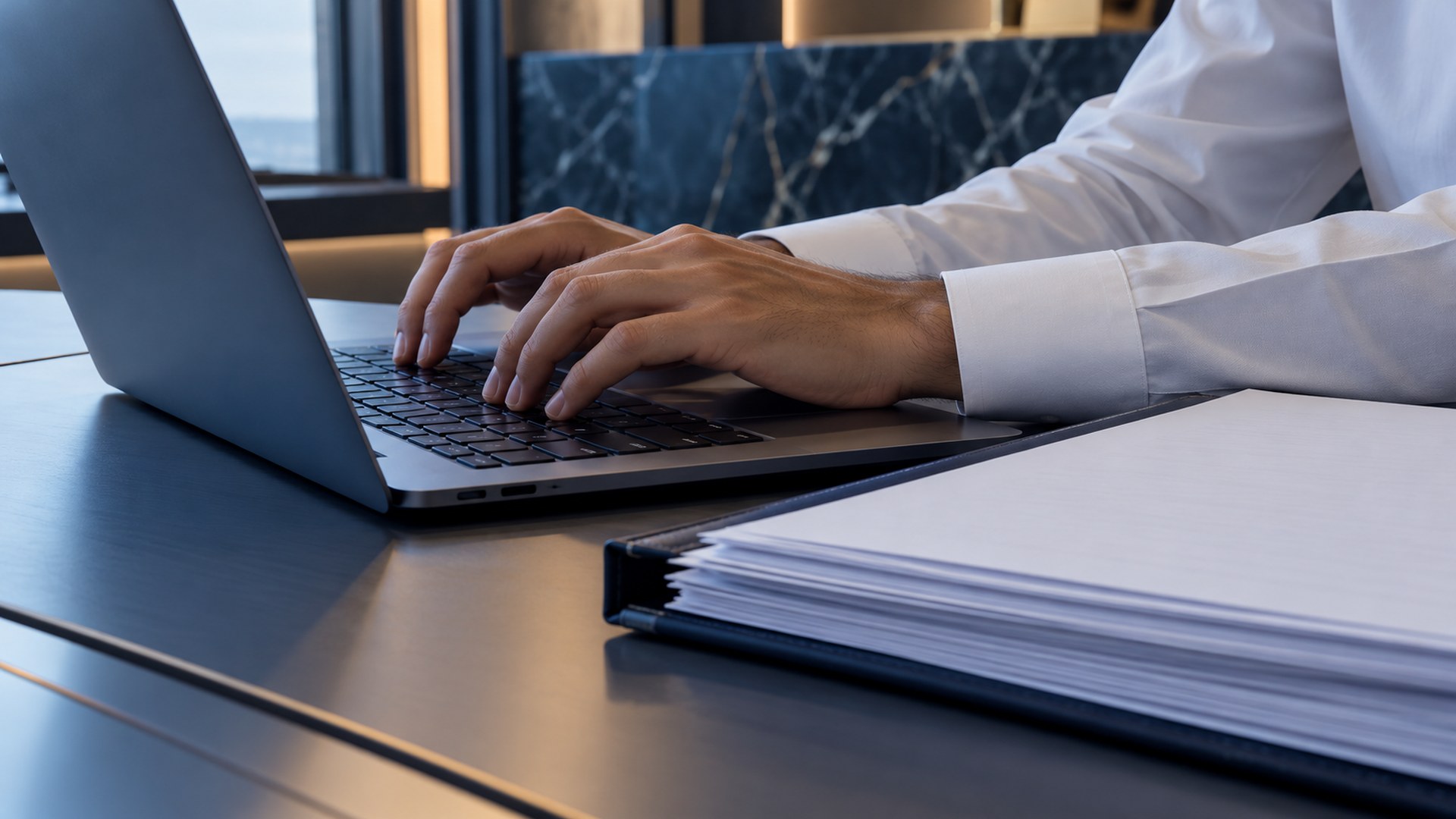 يدان تكتبان على لابتوب بجانب ملف أوراق مالية مرتب