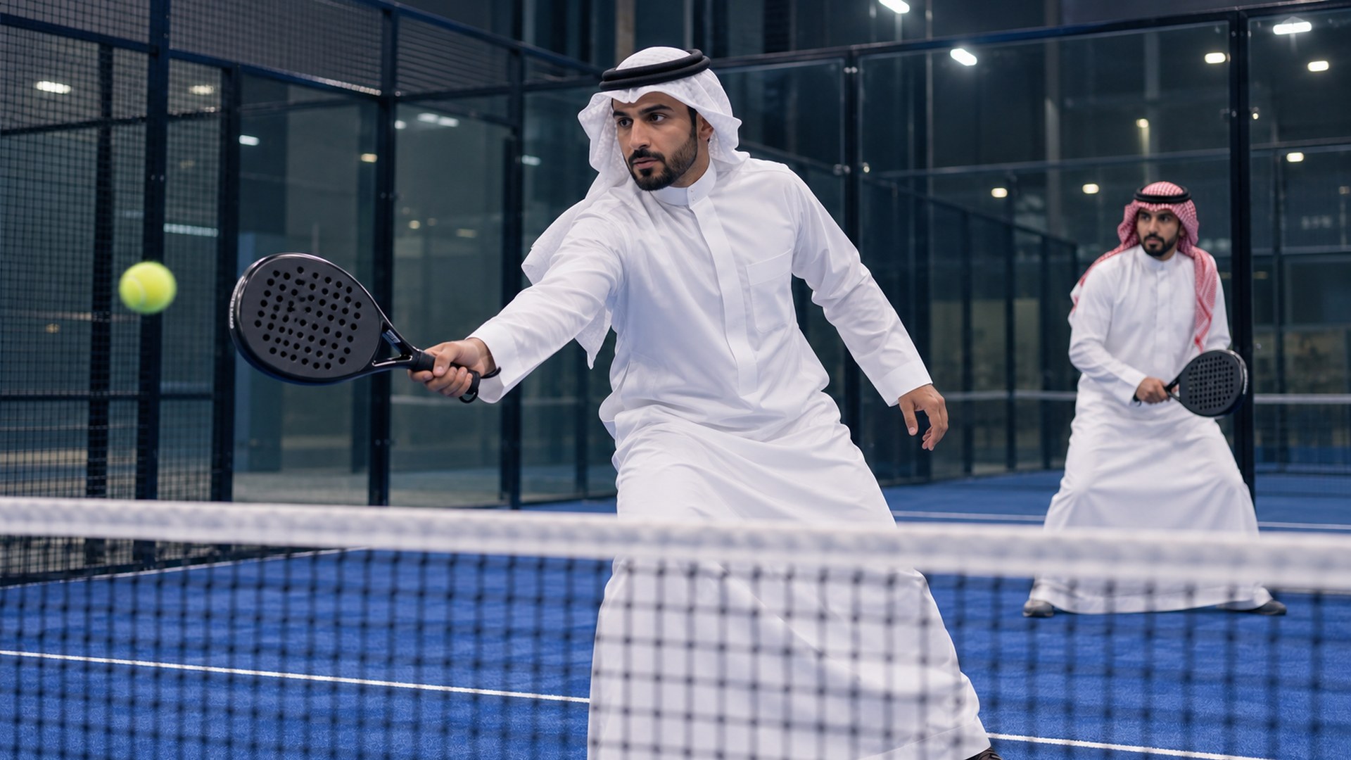 رجلان سعوديان يلعبان مباراة بادل ودية في ملعب داخلي مضيء