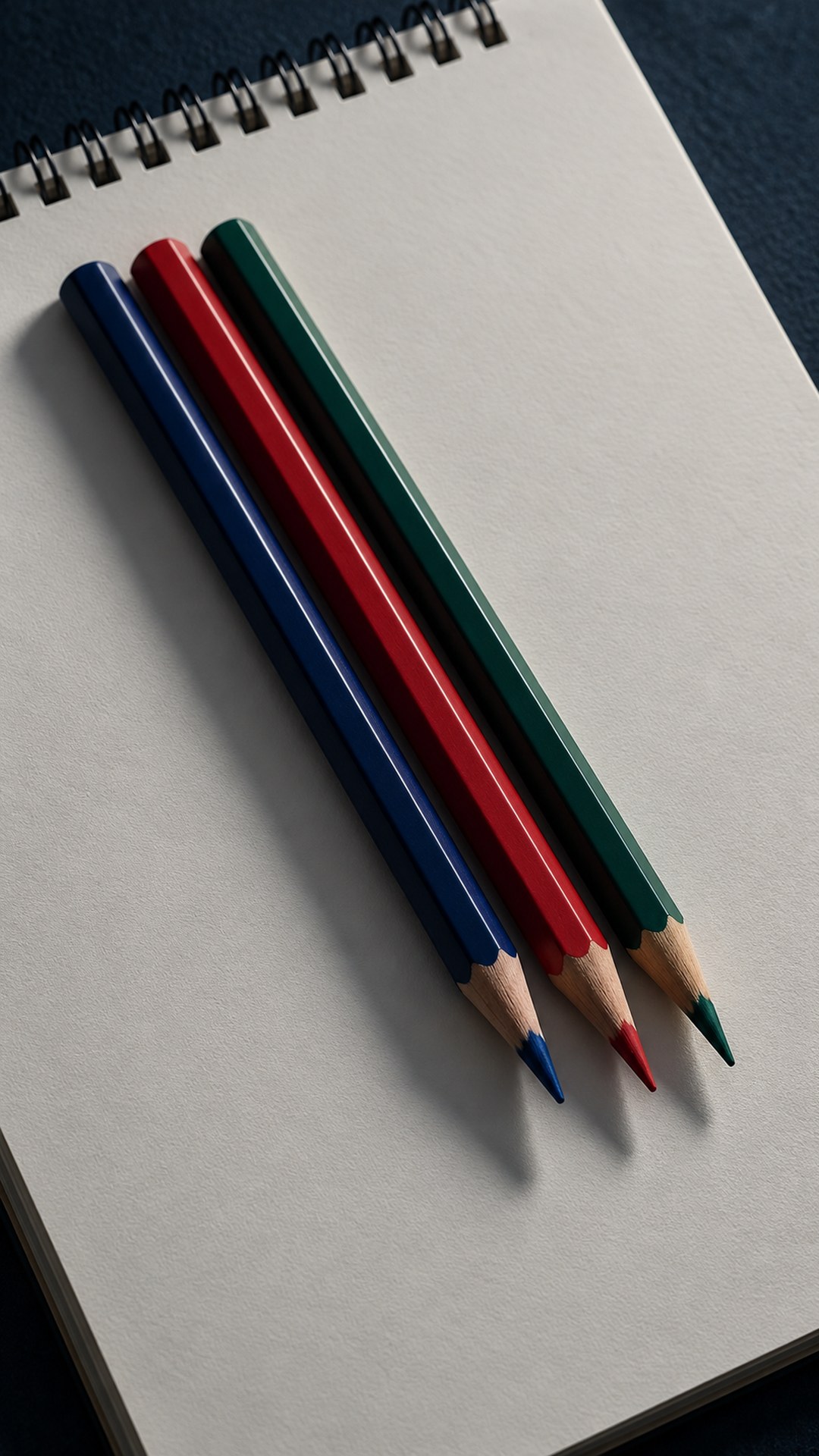 ثلاثة أقلام بألوان مختلفة على كراسة رسم فارغة