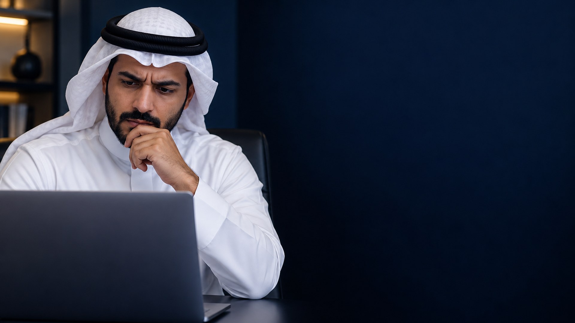 صاحب عمل سعودي محتار أمام اللابتوب في مكتب بسيط