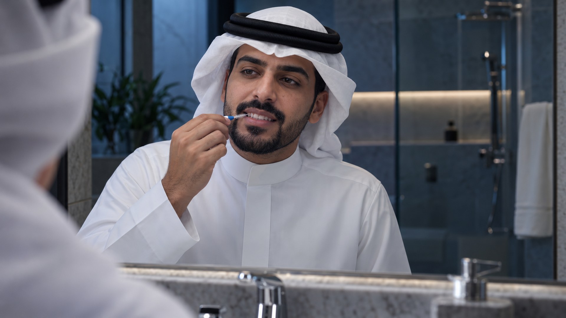 رجل سعودي ينظف بين أسنانه بفرشاة ناعمة أمام مرآة الحمام