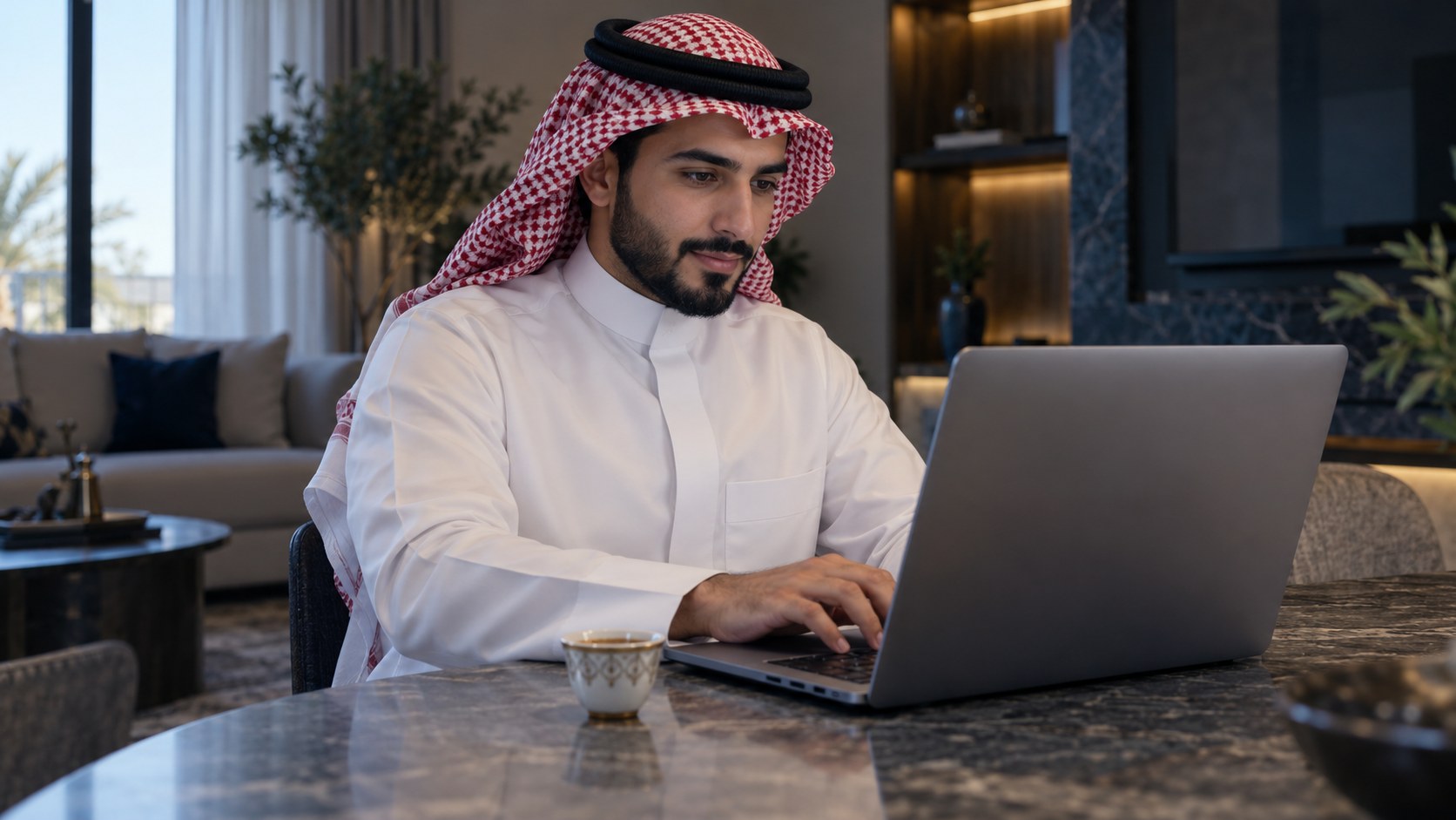 رجل سعودي يعبّي طلباً إلكترونياً على لابتوبه في البيت وبجانبه قهوة عربية