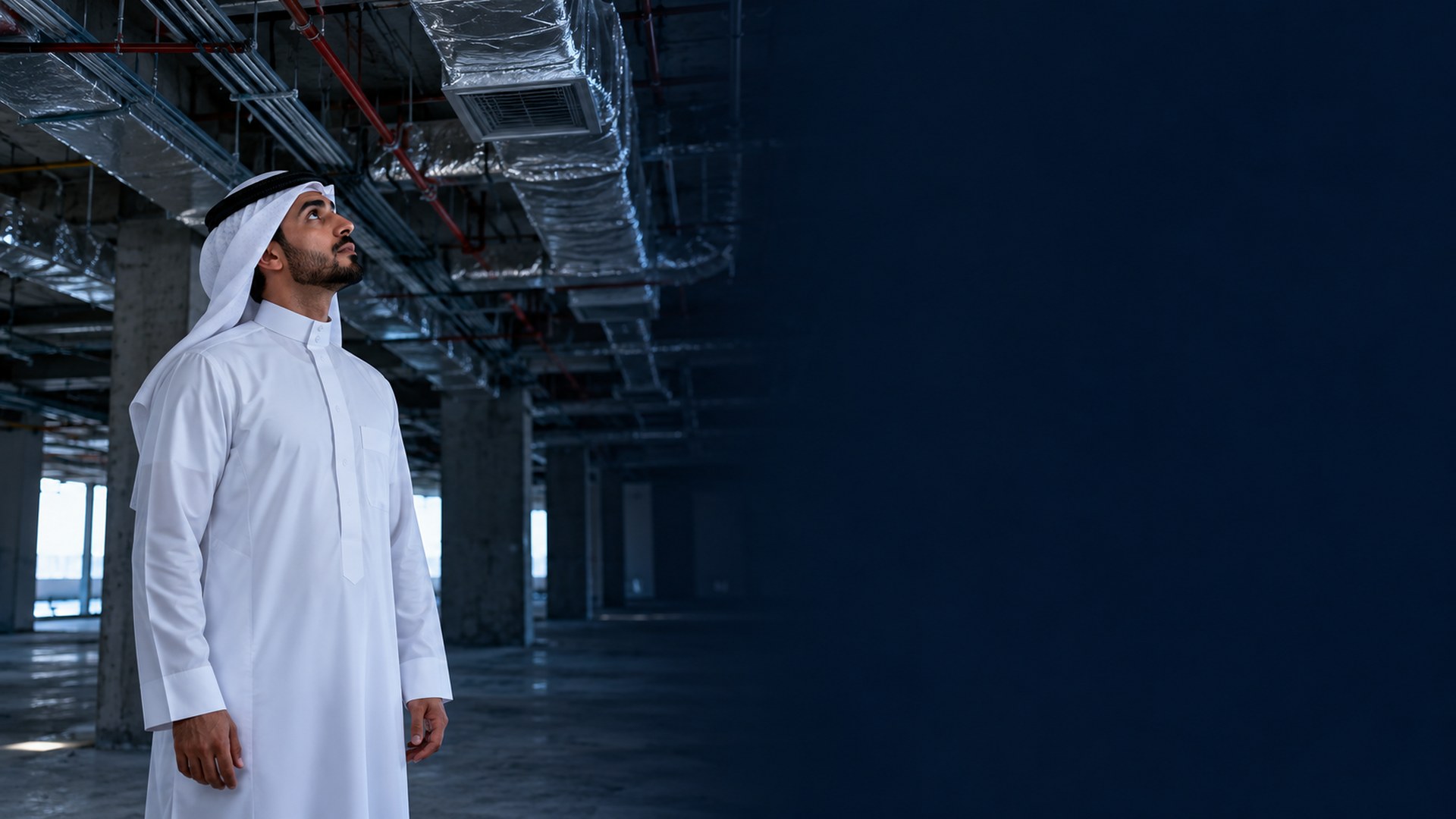 رجل سعودي بثوب أبيض داخل مبنى تجاري غير مكتمل ينظر لمجاري التهوية والأنابيب