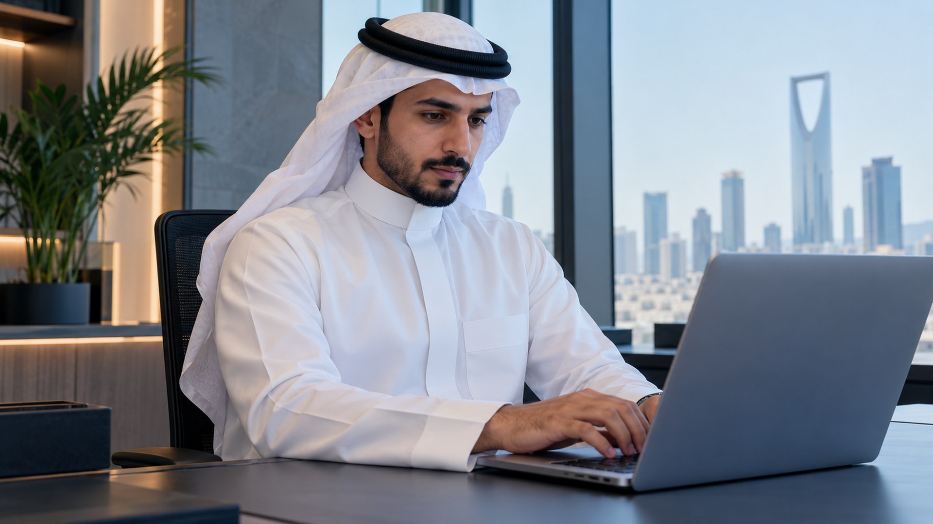 رجل سعودي بالثوب يكتب مقالاً على لابتوب حديث في مكتب مضيء