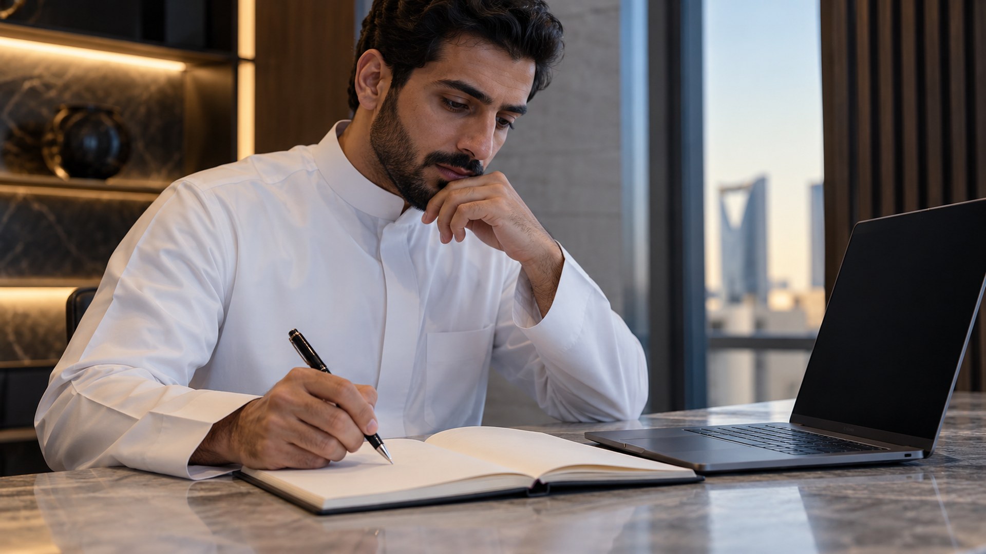 موظف سعودي يخطط لهدف تعليمي في دفتر بجانب اللابتوب