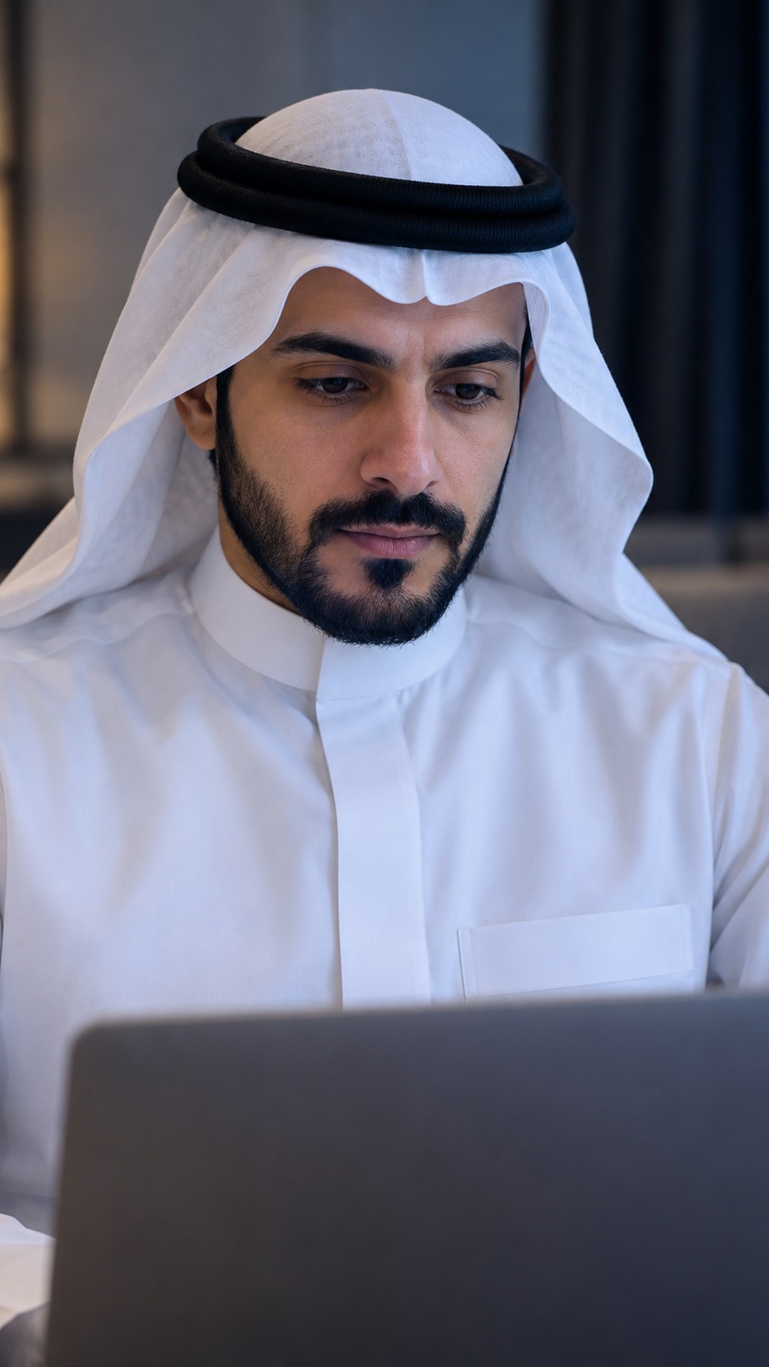 رجل سعودي متحفظ أمام لابتوبه في غرفة خاصة هادئة
