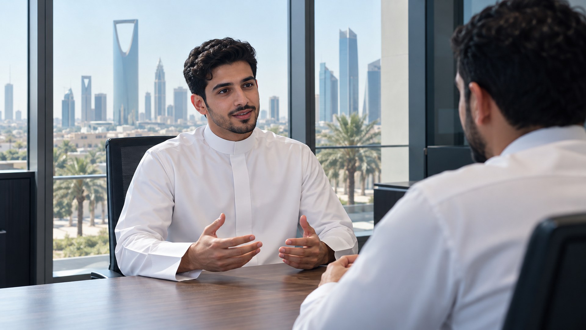 شاب سعودي يتحدث بثقة مع المحاور في مقابلة عمل بمكتب حديث
