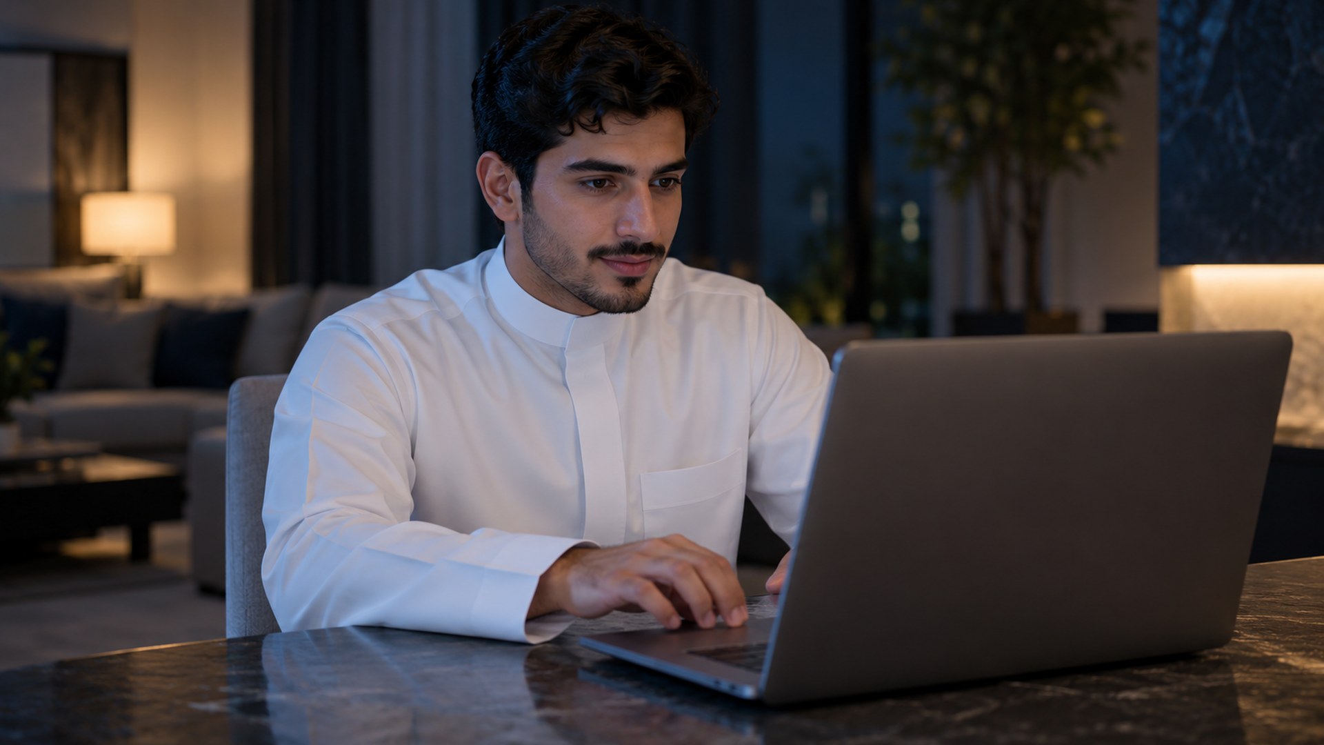 شاب سعودي بالثوب يفتح موقعاً على لابتوبه في البيت وإصبعه على لوحة اللمس