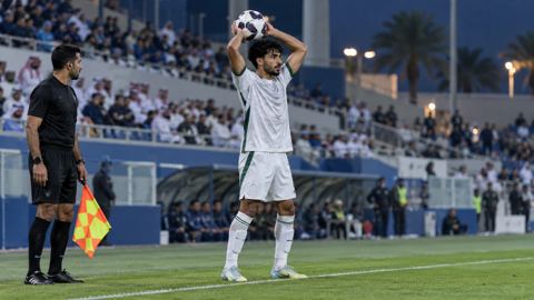 لاعب على خط التماس يمسك الكرة لرمية تماس والحكم يراقب
