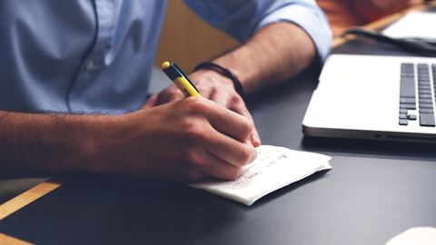 يد تكتب ملاحظات على ورقة بجانب لابتوب على مكتب داكن