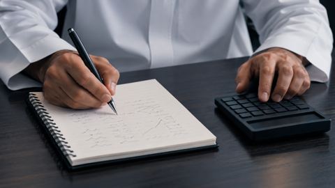 يدان تحسبان تكاليف المشروع والمصاريف وهامش الربح في مفكرة بجانب آلة حاسبة