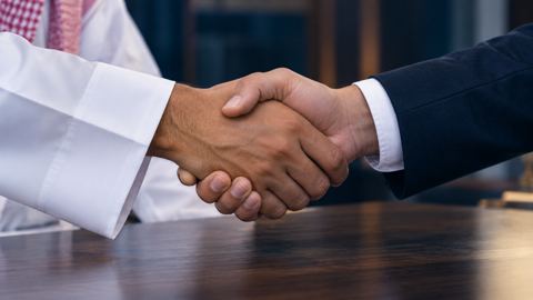 يدان تتصافحان بقوة فوق مكتب وإحداهما بكم الثوب