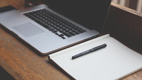 لابتوب ودفتر مفتوح وقلم على مكتب خشبي