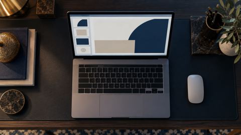 لابتوب يعرض تصميم عرض تقديمي بجانب فأرة على مكتب منزلي، من الأعلى