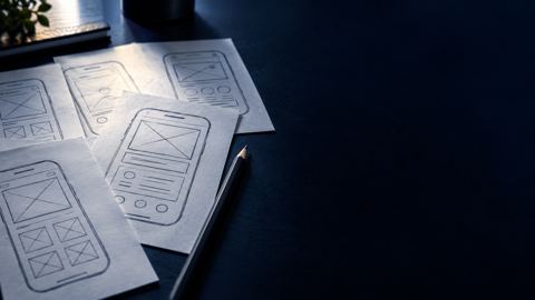 رسومات ورقية لشاشات جوال منتشرة على مكتب بجانب قلم رصاص