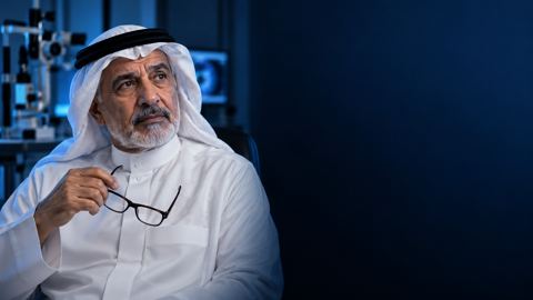 رجل سعودي كبير بالغترة والثوب يمسك نظارته متأملاً في عيادة عيون