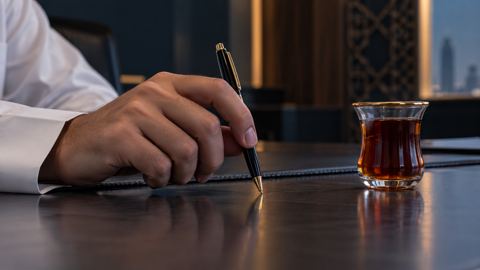 يد قلقة تنقر بالقلم على المكتب بجانب كوب شاي لم يُلمس