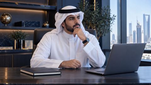 صاحب عمل سعودي يخطط بتفكير على مكتبه أمام دفتر مغلق ولابتوب