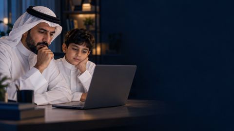 أب سعودي يتأمل اللابتوب بجانب طفله على مكتب المذاكرة