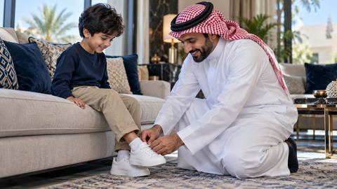 أب سعودي يجثو ليساعد ابنه الصغير في لبس حذاء رياضي مريح