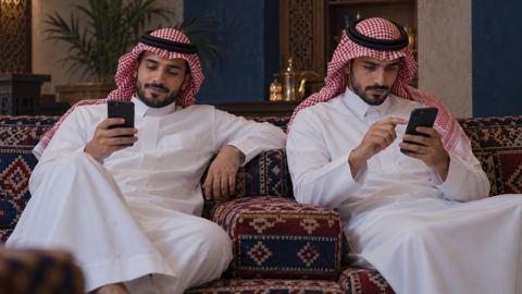 صديقان سعوديان على مسند في المجلس، كل منهما على جواله