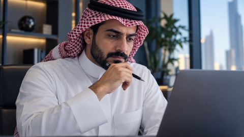 رجل سعودي يمسك قلماً ويتوقف متأملاً أمام بيانات على اللابتوب