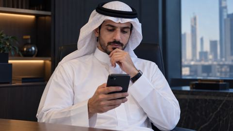 رجل سعودي يتريث قبل أن يحوّل من جواله في مكتب هادئ