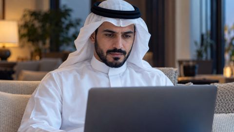 رجل سعودي يقرأ إعلاناً مالياً رسمياً على اللابتوب في البيت
