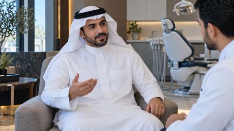 رجل سعودي يناقش ابتسامته مع طبيب الأسنان في غرفة استشارة هادئة