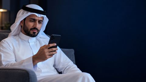 رجل سعودي على الكنب والجوال في يده بنظرة مترددة