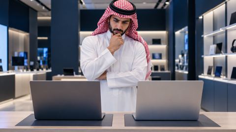 رجل سعودي في متجر إلكترونيات يقارن بين جهازي لابتوب