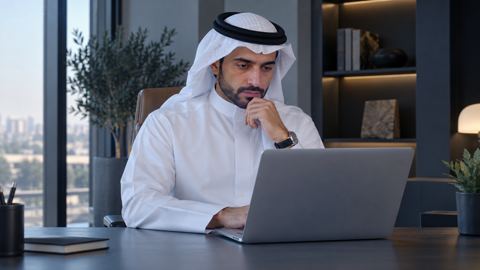 موظف سعودي يقرأ مقالاً على اللابتوب بتأمل في مكتب هادئ