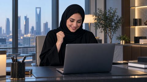 امرأة سعودية في مكتبها تبتسم أمام اللابتوب بعد اجتيازها اختباراً مهنياً