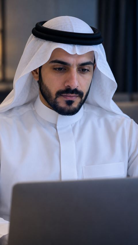 رجل سعودي متحفظ أمام لابتوبه في غرفة خاصة هادئة
