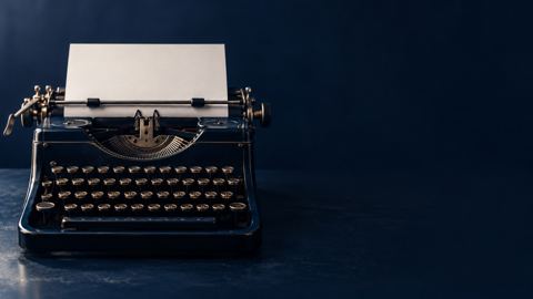 آلة كاتبة قديمة فيها ورقة بيضاء على مكتب كحلي