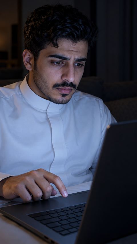 شاب سعودي متردد أمام اللابتوب ليلاً يفكر ماذا يكتب