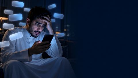 شاب سعودي بثوب أبيض يمسك جواله ليلاً وتحيط به فقاعات إشعارات كثيرة