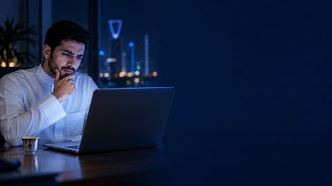 شاب سعودي محتار أمام لوحة تحليلات على لابتوبه ليلاً وبجانبه قهوة عربية