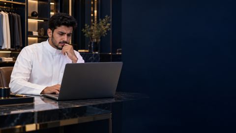 صاحب محل سعودي شاب وحيد في بوتيكه الأنيق الفارغ في الرياض محتاراً أمام لابتوبه